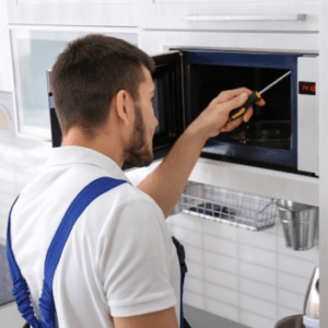 a man in overalls using a screwdriver to open a microwave