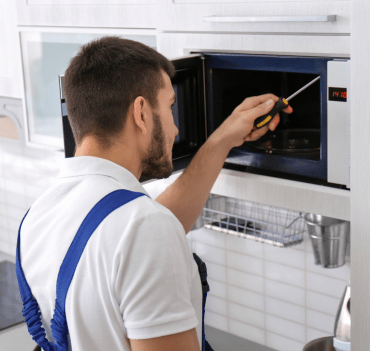 a man in overalls using a screwdriver to open a microwave